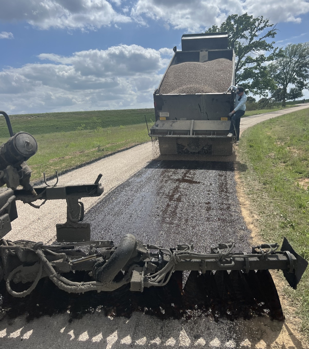 Chip seal aggregate spreader laying down stone over fresh emulsion